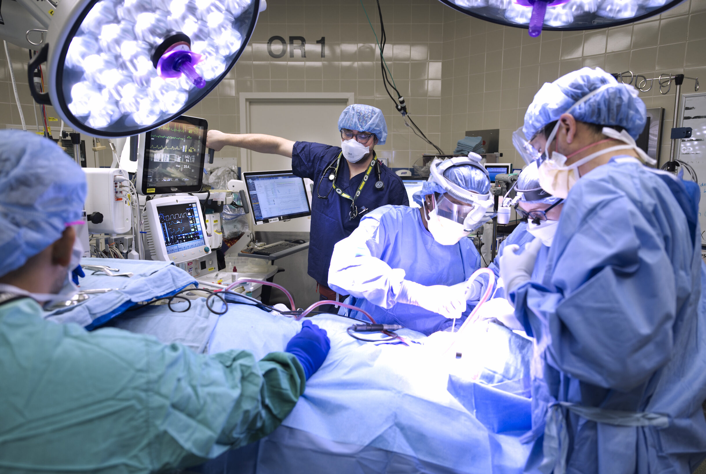 four medical personnel wearing blue scrubs surrounding a patient in the operating room