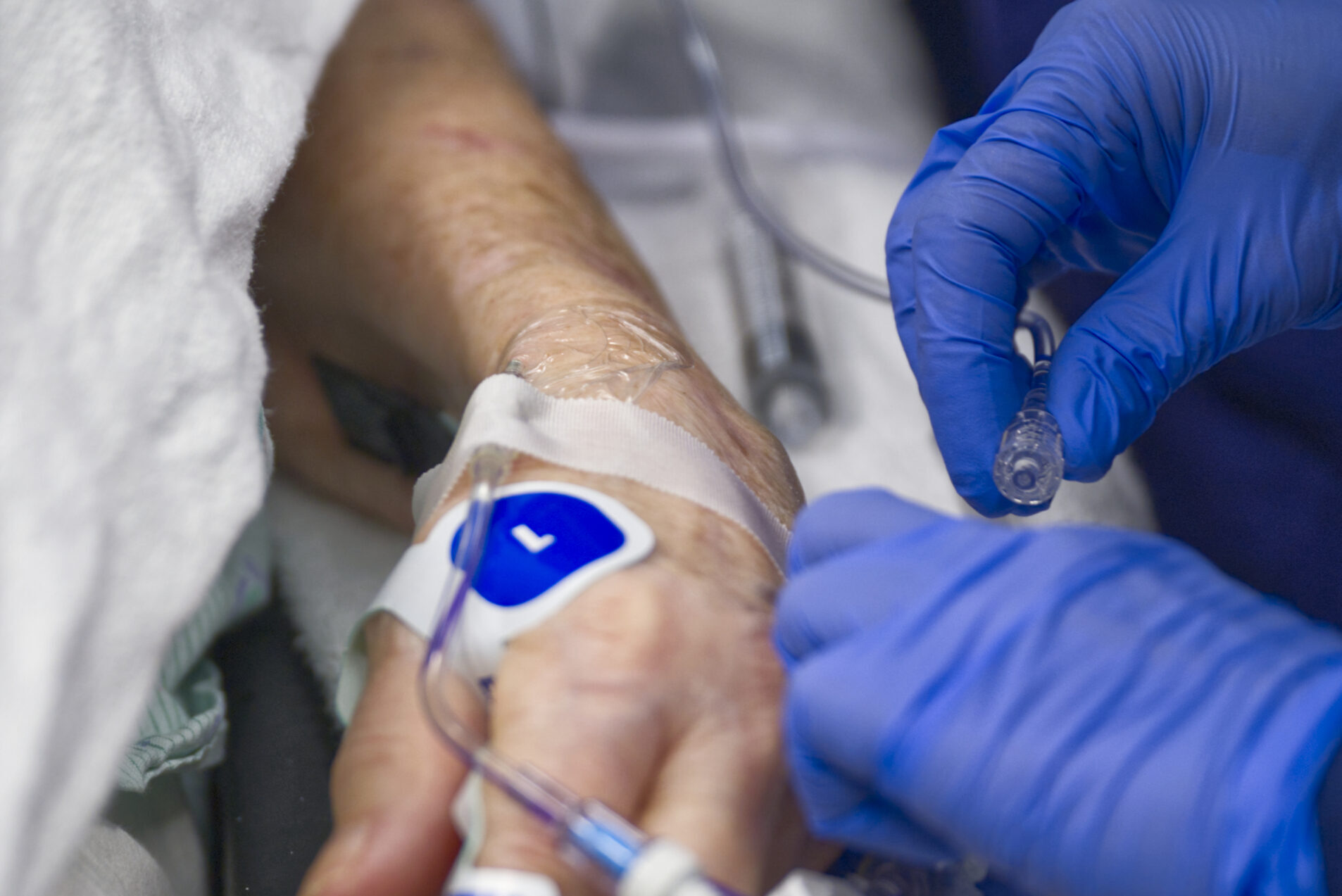 blue gloved hands attaching a catheter to a patient's wrist