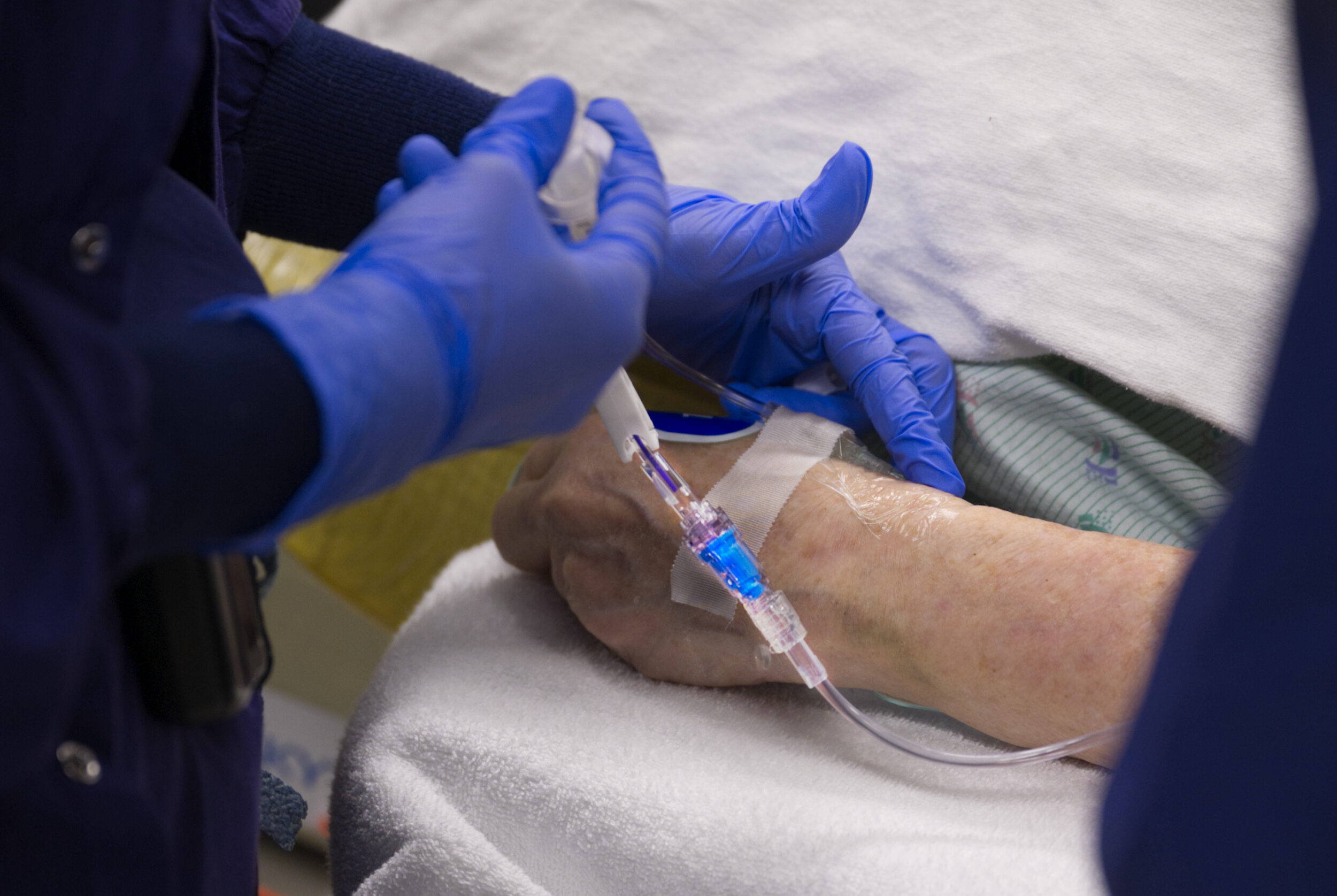 blue gloved hands holding a catheter attached to a patient's wrist