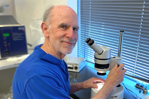 Dr. Morgan wearing a blue shirt, smiling and sitting with a microscope
