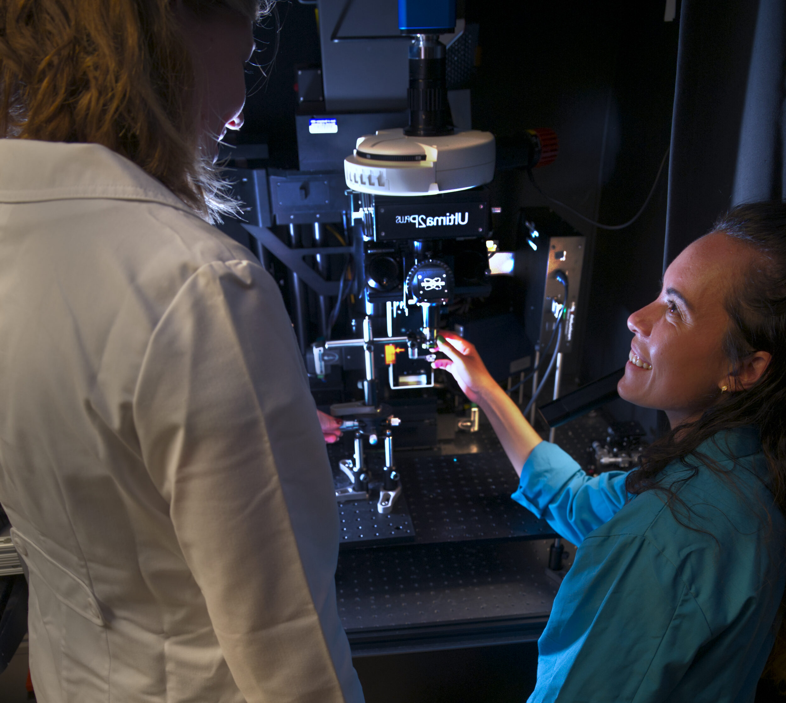 female graduate student sitting at electron microscope with another student observing