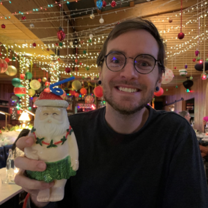 Adam holding a Santa ornament with Christmas lights in the background.