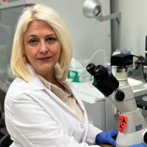Blonde woman wearing white lab coat using a microscope. 