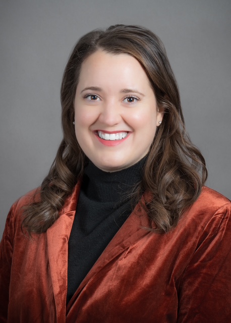 Headshot portrait of a woman with brown hair in an orange suit jacket