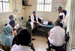 Doctors in lab coats and scrubs in a classroom learning session.