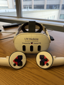 A headset and two hand controls imprinted with the UW Medicine and Vantari VR logos sits on a table by a window.