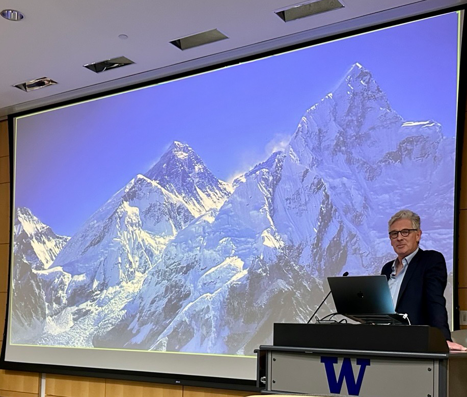 Dr. Mike Grocott standing at a lecturn. The large screen behind him projects a photo of Mt. Everest.