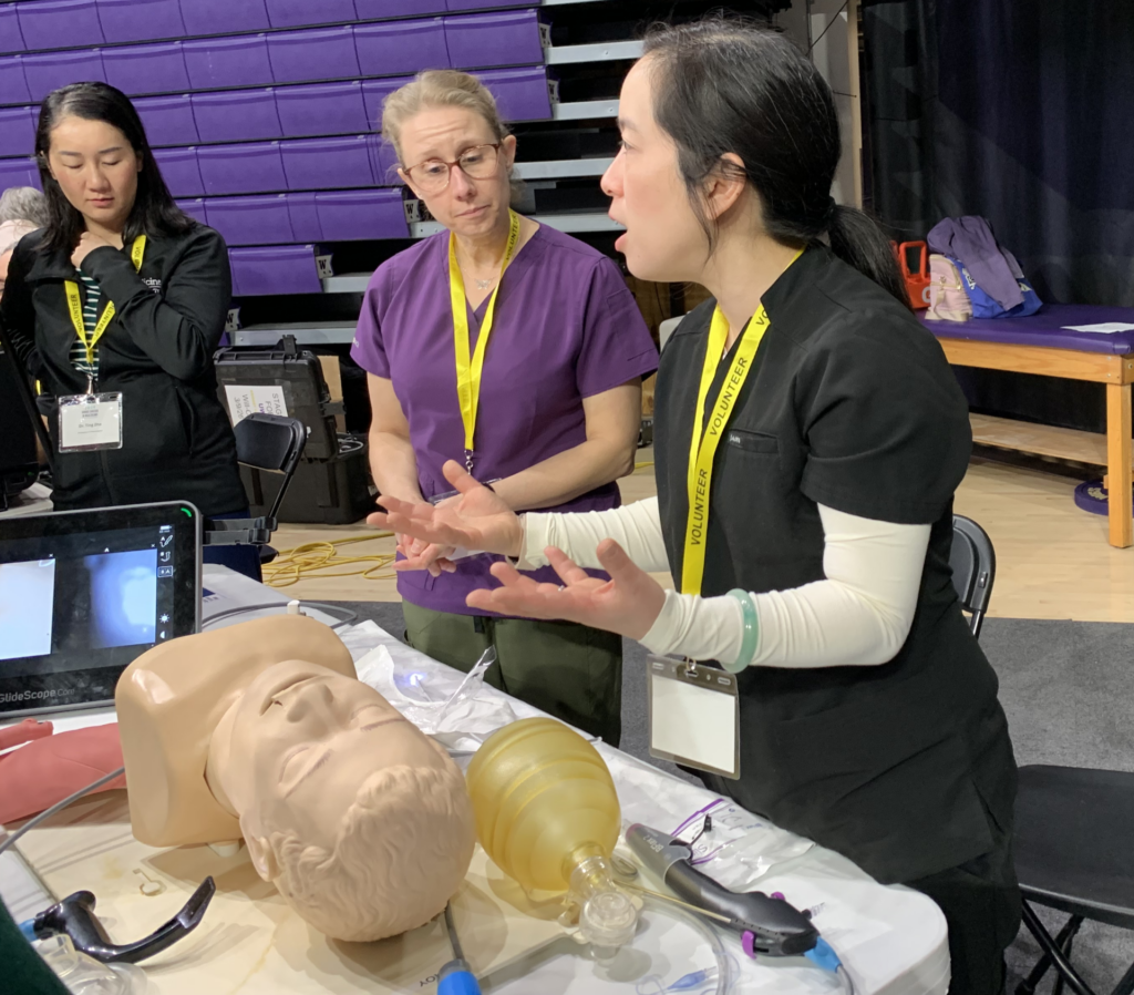 A woman provider explains airway management while standing next to a CRNA and another doctor.
