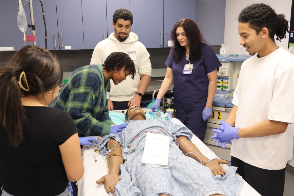 A young woman leans over a manikin during a procedure simulation.