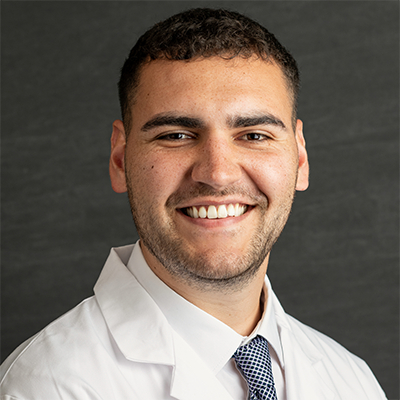 Smiling person with short dark hair in doctor's coat.