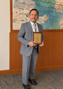 Dr. Sharma holding his award plaque in a conference center hallway